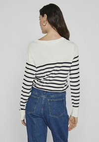 Jersey a rayas con rayas horizontales en blanco y negro, escote redondo y mangas largas, combinado con jeans de mezclilla azul de cintura alta.