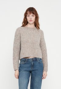 Adīta džemperis bēšā krāsā ar daudzkrāsainiem punktiņiem, ar apaļu apkakli un nokrītām plecu šuvēm. Savairots ar zilām džinsām.