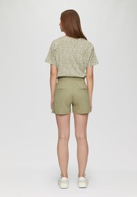 Lichtgroen gestreept T-shirt met korte mouwen en witte stippen, in combinatie met olijfgroene shorts. De shorts hebben twee achterzakken en een elastische tailleband.