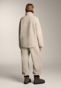 Bež pulover iz flisa z visokim ovratnikom, kombiniran z usklajenimi flis hlačami z ohlapno zasnovo. Rjavi gležnarji s krznenimi detajli.