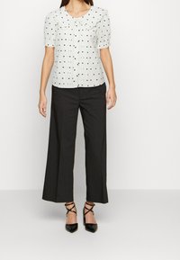 Vit blus med svarta prickar, stor krage, korta puffärmar. Kombinerad med högmidjade, vida svarta byxor och svarta spetsiga klackar.