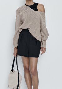 Beige suuri neulepaita, musta tiukka minihame, pitää beigeä laukkua, jossa on mustia yksityiskohtia. Sileä rakenne kerrostetuilla suunnitteluelementeillä.