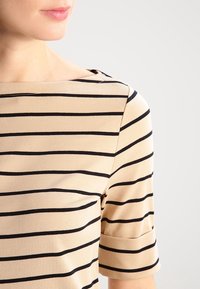 Beige striped top with black horizontal lines, featuring a square neckline and short sleeves. The fabric appears soft and smooth.