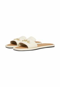 Chanclas de color crema con una textura suave, que cuentan con una amplia correa y un detalle de hardware dorado. La suela es plana con un borde negro.