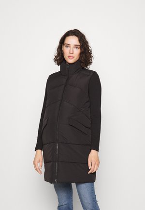 Svart polstret vest med høy krage, glidelås og to frontlommer. Glatt tekstur med horisontale sømmer og lagdelt design.