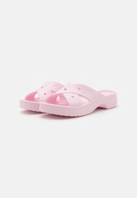 Des sandales en caoutchouc roses avec une semelle intérieure texturée, un design de bride croisée et des perforations pour la respirabilité.