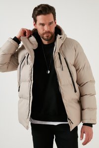 Giacca puffer beige con cappuccio, dotata di cerniere e dettagli neri. Realizzata in materiale liscio e trapuntato, ha una vestibilità comoda e tasche.