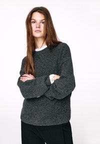 Maglione grigio lavorato a maglia con maniche lunghe e scollo rotondo. Indossato sopra una camicia bianca, presenta una vestibilità comoda e una texture morbida.