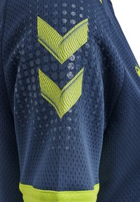 Navyblauer atmungsaktiver Stoff mit erhabenen Punkten zeigt zwei gelbe Chevronstreifen mit feinen parallelen Linien, über einem gelben Stoffsaum.