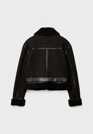 Veste en shearling noir avec des détails en faux cuir, large col et poignets retroussés, vue de dos sur un fond gris clair.