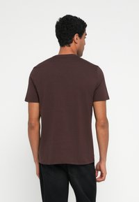 Καφέ κοντομάνικη μπλούζα �με στρογγυλή λαιμόκοψη, κατασκευασμένη από απαλό ύφασμα, με λεία υφή και ίσια γραμμή. Ορατά ράμματα στο τελείωμα.