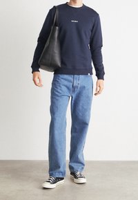 Felpa della marina con logo "LES DEUX", jeans blu e borsa tote nera. Sneakers in tela nera con suole bianche, forma rettangolare, design minimale.