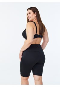 Reggiseno sportivo nero con spalline regolabili e chiusura a gancio, abbinato a pantaloncini da ciclismo neri a vita alta. Tessuto liscio, design aderente.
