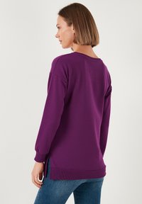 Felpa viola dal taglio rilassato, maniche lunghe, spacchi laterali e orlo a coste. Tessuto morbido, design minimalista.