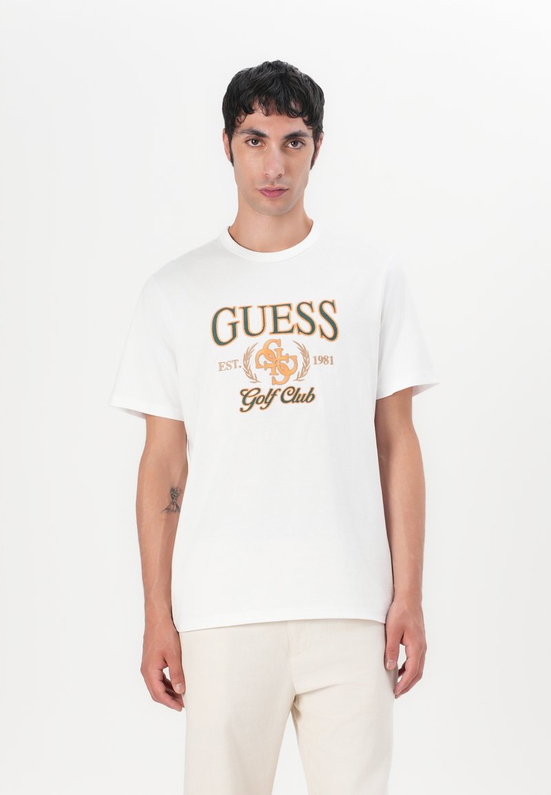Camiseta blanca de algodón con el logo impreso "GUESS Golf Club" en naranja y negro. Mangas cortas, escote redondo, ajuste relajado.