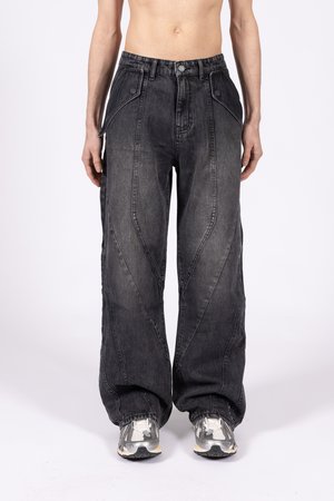 Ohlapne črne jeans hlače iz denima, ki vključujejo poševne šive in zbledele površine. V kombinaciji s sivimi športnimi čevlji.