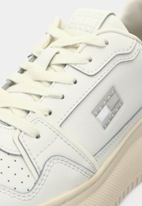 Weiße Ledersneaker mit durchgestochenen Akzenten, flachen Schnürsenkeln und einer grauen Gummisohle. Enthält ein silbernes Logo-Emblem an der Seite.