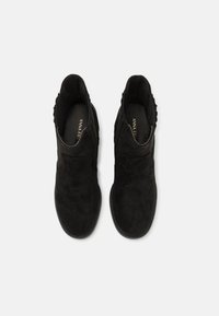 Bottines en daim noir avec une semelle plate, présentant une finition lisse et des panneaux latéraux élastiques pour un enfilage facile. Aucun accessoire supplémentaire visible.