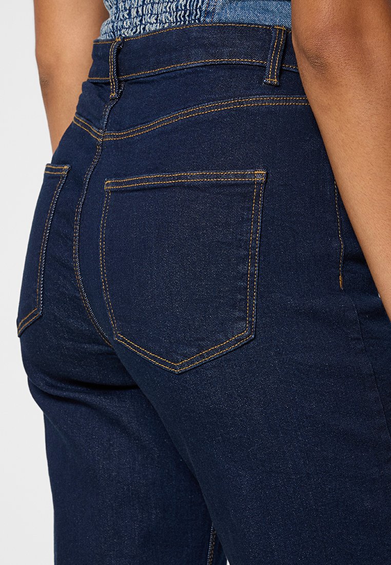 Dunkelblaue Denim-Jeans mit glatter Textur, zwei Gesäßtaschen mit gelben Nähten und einem klassischen Hochbund-Design.