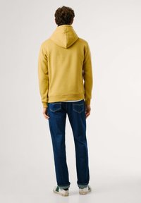 Yellow hoodie with a drawstring hood, ribbed cuffs, and hem, paired with blue denim jeans and white sneakers. Plain background.