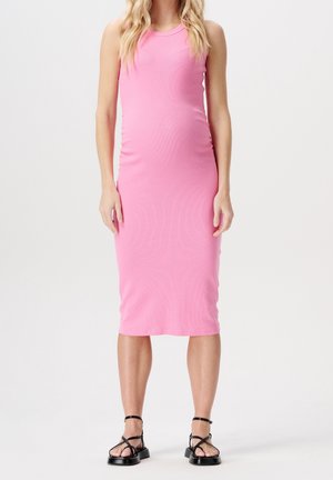 Femme portant une robe midi rose ajustée sans manches avec des sandales noires à brides, debout devant un fond blanc uni.