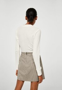 Camiseta de manga larga blanca acanalada combinada con una falda mini a cuadros marrón y blanca, con una cremallera en la parte posterior y un corte ajustado.