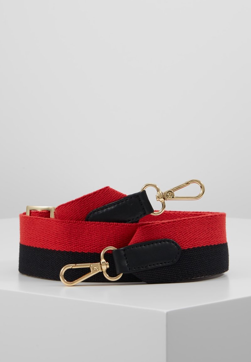 Sangle de sac ajustable rouge et noire avec des fermoirs en métal doré et des connecteurs en cuir noir, enroulée sur une surface blanche.