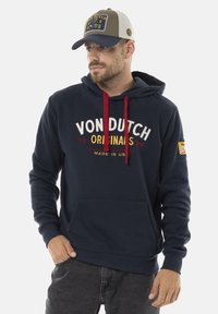 Sweatshirt à capuche marine avec des cordons rouges, poche kangourou à l'avant et lettrage blanc. Assorti à une casquette grise et beige avec un logo.