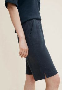 Navy blue linen blend shorts with a relaxed fit, tapered leg, side pockets, and a subtle slit at the hem for ease of movement.