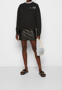 Sudadera negra de gran tamaño, falda mini de cuero, bolso azul y blanco con estampado, y sandalias negras con detalles dorados.