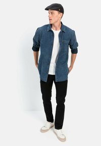 Blauw geruit overhemd met opgerolde mouwen, wit T-shirt, zwarte broek en lichtgekleurde sneakers, gecombineerd met een zwarte pet.