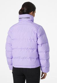 Veste matelassée de couleur violet clair avec des coutures horizontales, un col montant et un logo noir "Helly Hansen" au dos. Tissu lisse et isolant.