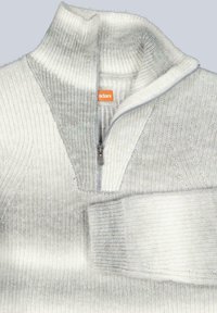 Hellgrauer Pullover mit hohem Kragen, halbem Reißverschluss, gerippter Struktur und sanftem Farbverlauf. Mit einem orangefarbenen Logetikett versehen.