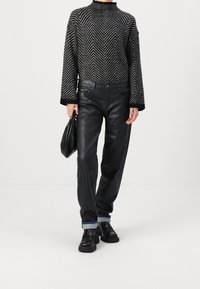 Suéter de patrón en espiga en blanco y negro con mangas largas, combinado con pantalones de cuero negro con dobladillo vuelto y un pequeño logo.