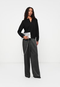 Zwarte lange mouwen top met V-hals, gecombineerd met losse, metallic grijze wijde broekspijpen. Houdt een zilveren clutch met een kettingband vast.