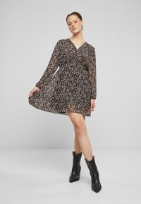 Black floral dress with long sheer sleeves, v-neckline, and a flowing skirt. Worn with black cowboy-style ankle boots.