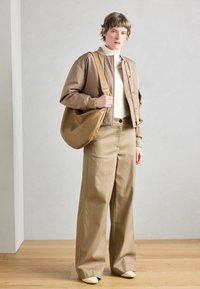 Rjava bomber jakna z rebrastimi manšetami, kremni pulover z dolgim vratom, široke rjave hlače in ohlapna rjava torba za čez ramo. Povsod gladke teksture.