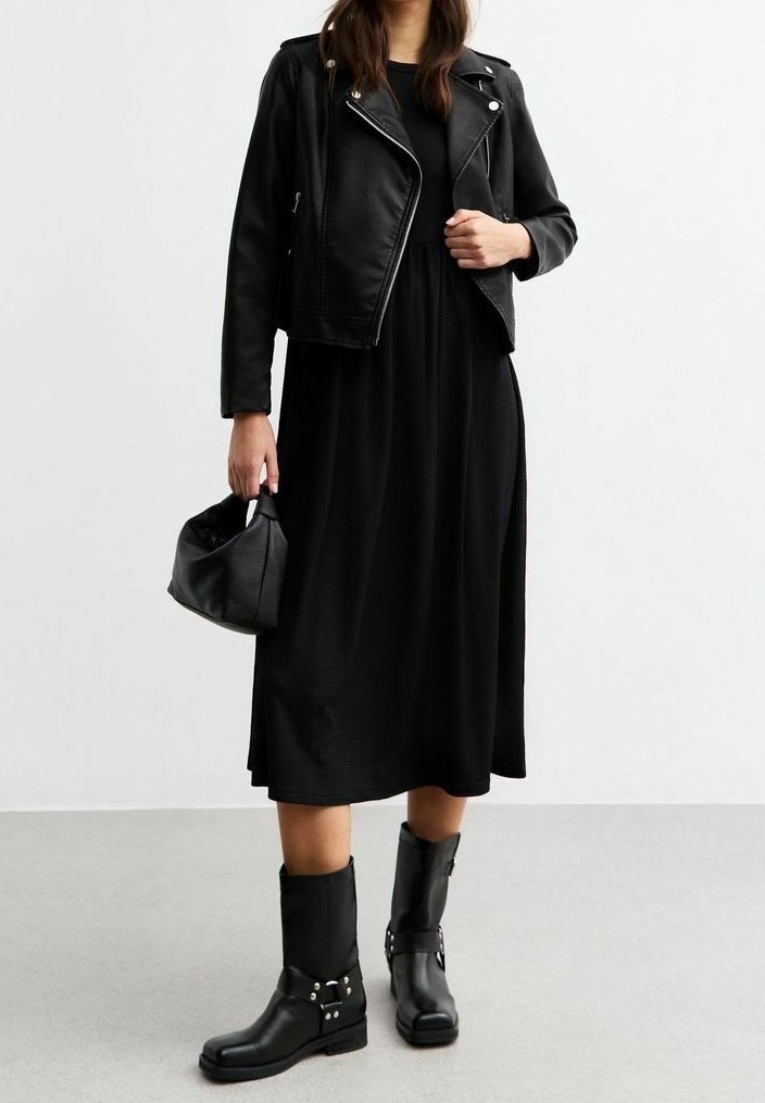 Musta nahkainen moottoripyörätakki mustan mekon päällä, yhdistettynä mustiin nilkkabootseihin, joissa on hopeisia yksityiskohtia. Kantaa pientä mustaa käsilaukkua.