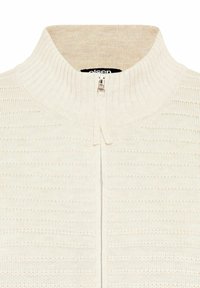 Helles, beiges Zip-Up-Sweatshirt mit geripptem Muster. Hat einen hohen Kragen und ein vertikales Streifenmuster auf dem Körper. Entworfen mit einem glatten Reißverschluss.