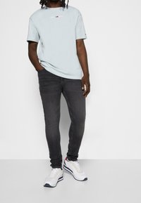 Camiseta de manga corta azul claro con un logo, acompañada de unos jeans ajustados gris oscuro y zapatillas blancas con detalles en azul marino y rojo.