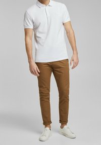 Vit polo-shirt med korta ärmar, ljusbruna slim-fit chinos och vita sneakers. Avslappnad stil med minimalistisk design. Inga synliga mönster eller logotyper.