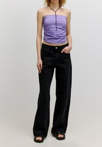 Lila Cropped-Top mit geraffter Textur, kombiniert mit hochgeschnittenen schwarzen weit geschnittenen Jeans. Modell trägt flache schwarze Sandalen.