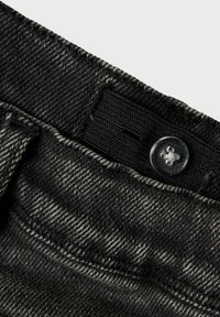 Tela de mezclilla negra con una superficie texturizada, que presenta un botón visible y un elástico en la cintura; la vista en primer plano resalta los detalles del cosido.