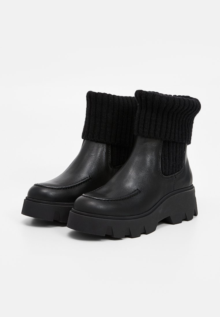 Schwarze Knöchelstiefel mit einer stabilen Sohle, aus Leder gefertigt und mit einem gerippten Strickbund versehen. Glatte Textur mit kontrastierenden Nähten.