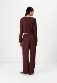 Burgundy cropped sweater with a textured finish, paired with high-waisted, wide-leg trousers. Designer footwear features a leopard print.