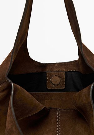 Brown suede tote bag with a circular snap closure, featuring a black interior lining and embossed branding on the inner side.