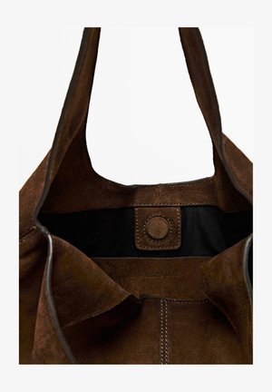 Brown suede tote bag with a circular snap closure, featuring a black interior lining and embossed branding on the inner side.