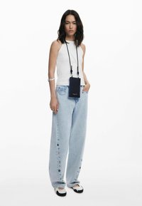 Vit ärmlös topp, ljusblå vida denimjeans med knapprutiner, och svart crossbody-väska med blå detaljer. Svart och vit sko.