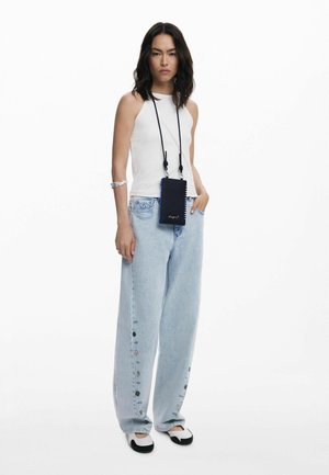 Top bianco senza maniche, jeans in denim azzurro chiaro a gamba larga con dettagli in bottone e pochette a tracolla nera con rifiniture blu. Scarpe in bianco e nero.