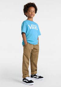 Modrý bavlněný tričko s velkým bílým logem "VANS", khaki kalhoty a černo-bílé tenisky se šněrovacím designem a klasickým vzorem.